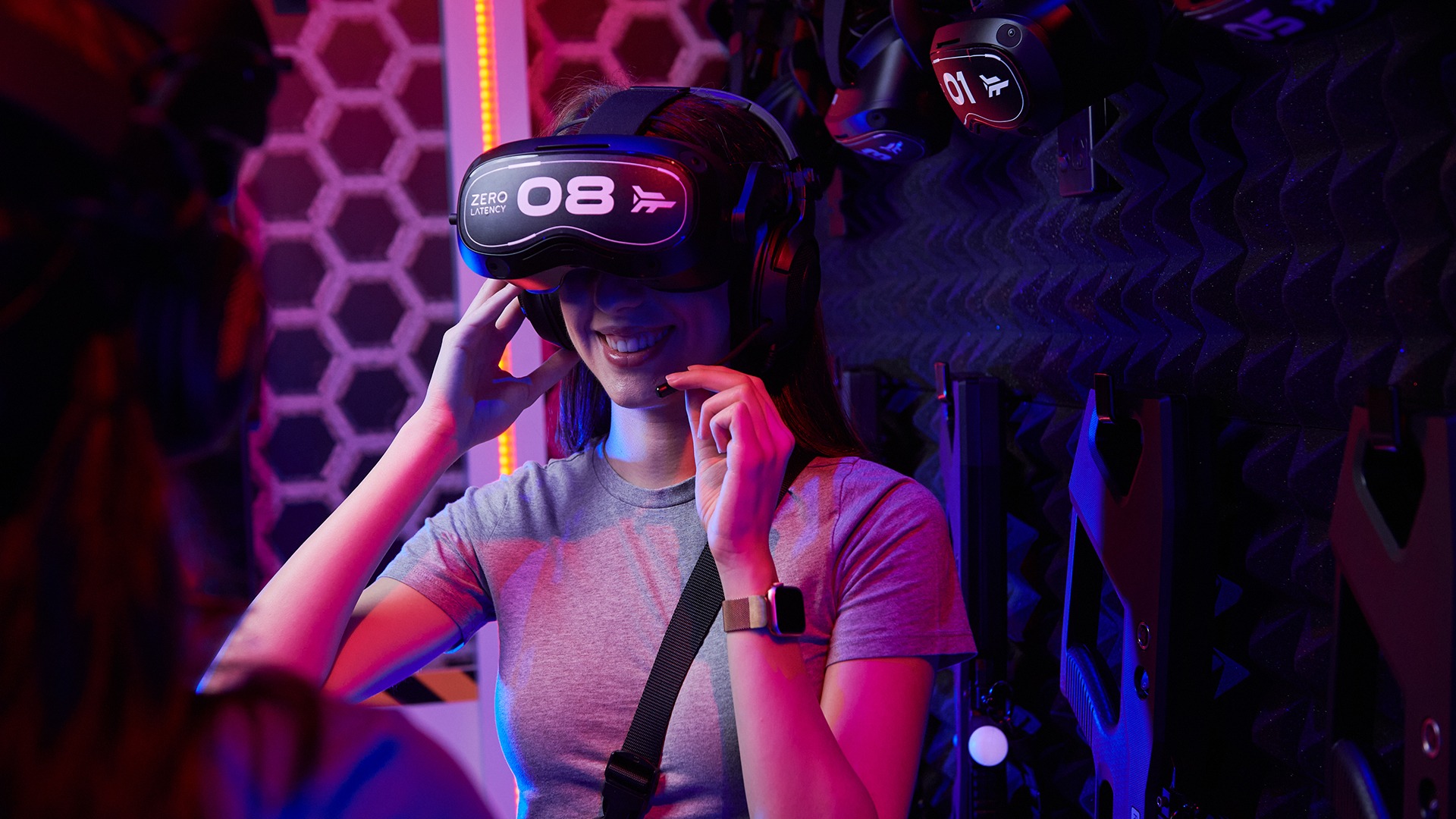 A Zero Latency VR guest smiling while adjusting a headset in the suit-up area